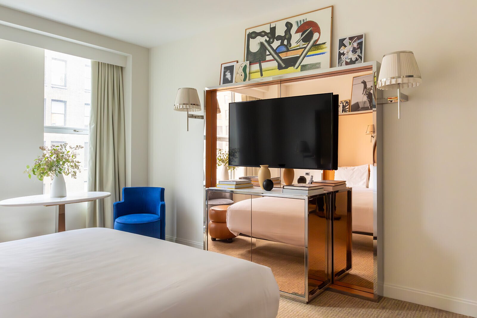 hotel room with a large bed, mirrored headboard, and a blue chair by a window with natural light.