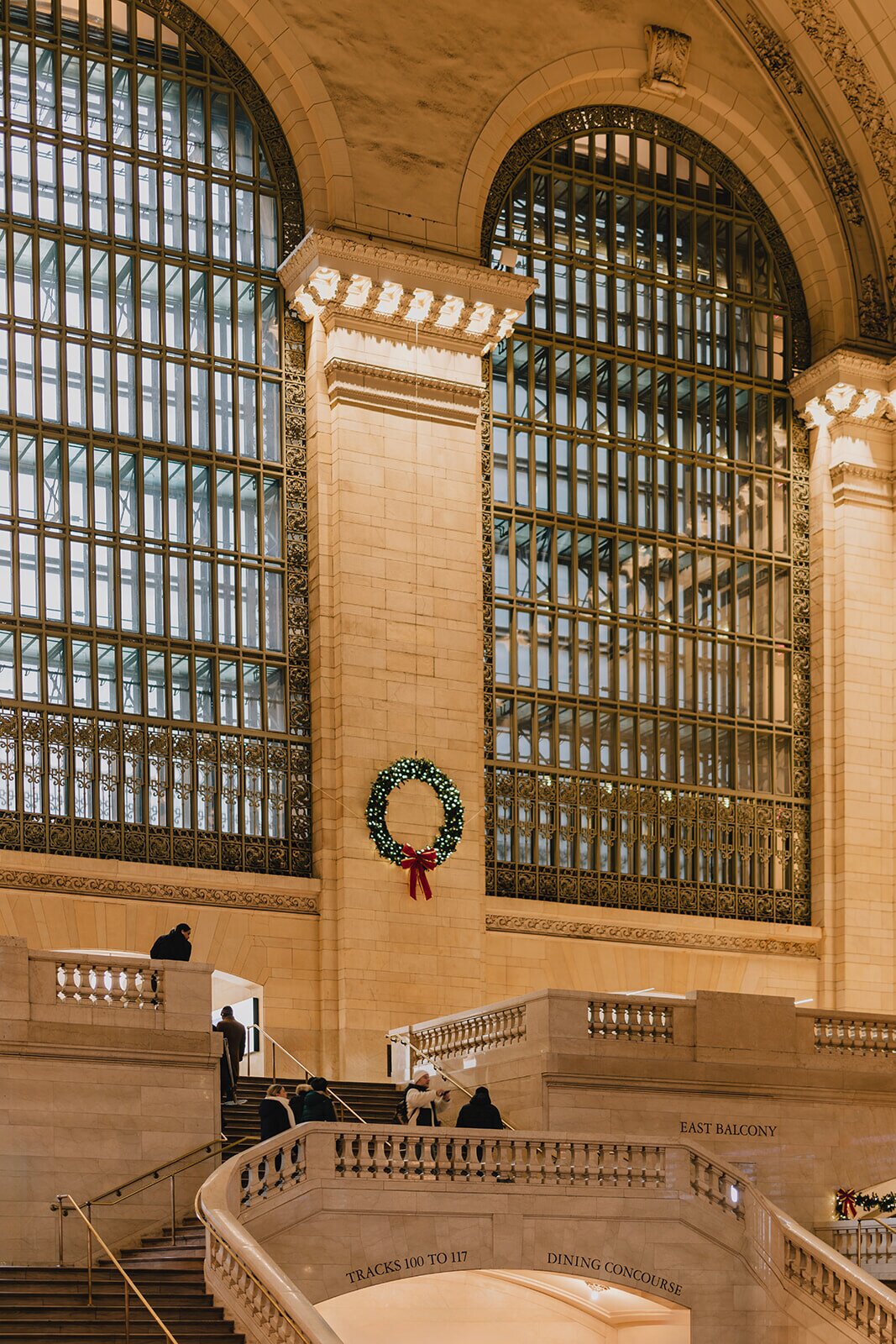 Grand Central Terminal interior during the holidays, with its iconic arched windows, marble staircases, and a glowing Christmas wreath decorating the main hall in New York City.